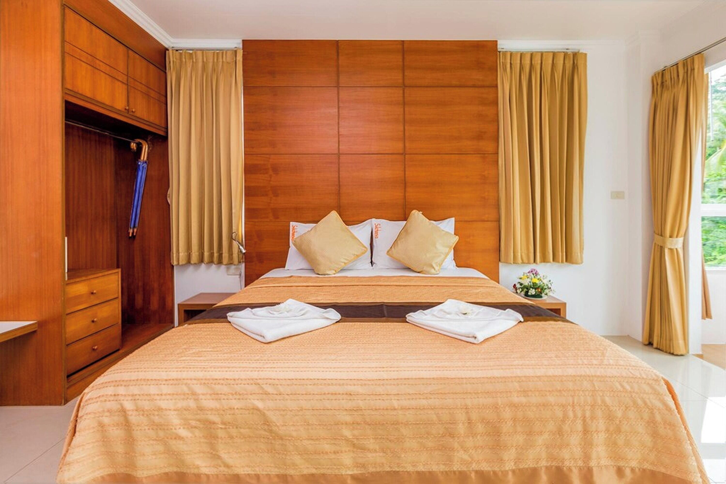 Een hotelkamer met een groot bed, een houten hoofdbord, beige gordijnen en een kledingkast.