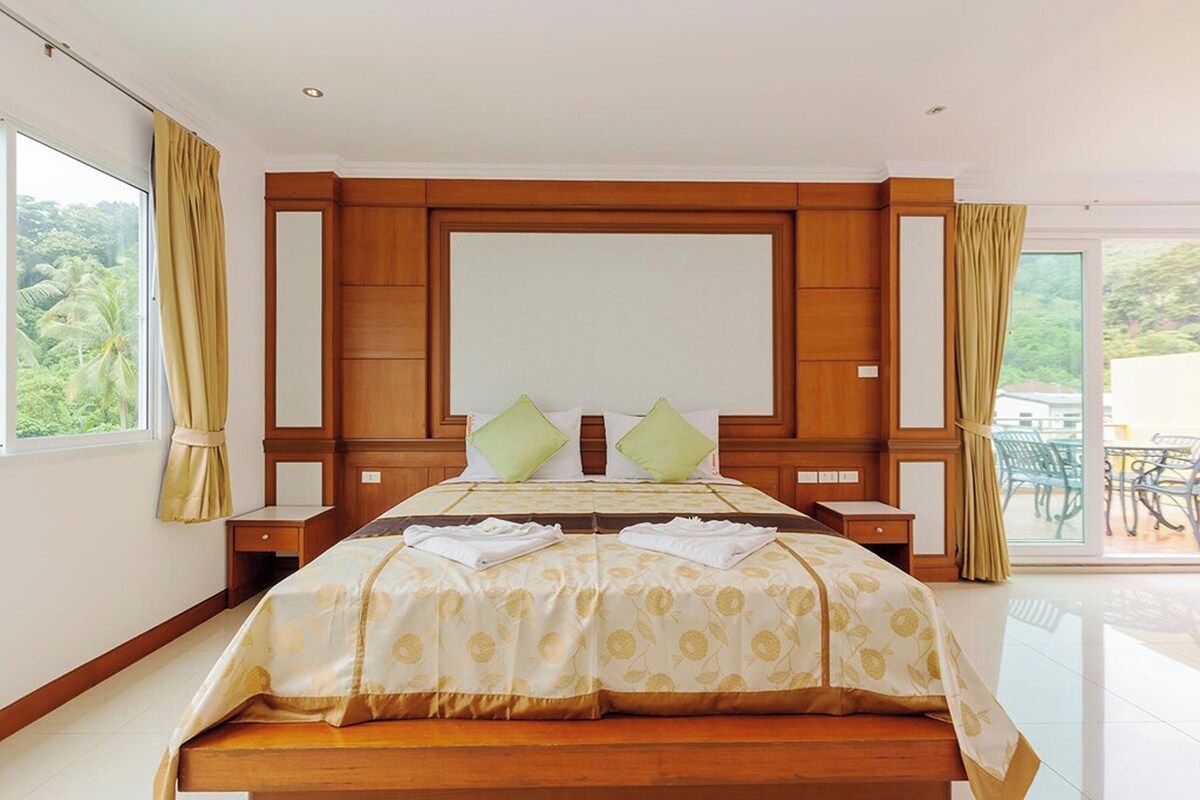 Habitación de hotel con una cama grande, cabecera de madera, dos mesitas de noche y vistas a zonas verdes.