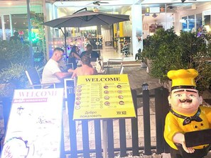 A restaurant entrance with a welcome sign, outdoor seating, and a decorative figure. - Sukcheewa Residence Phuket (Patong)
