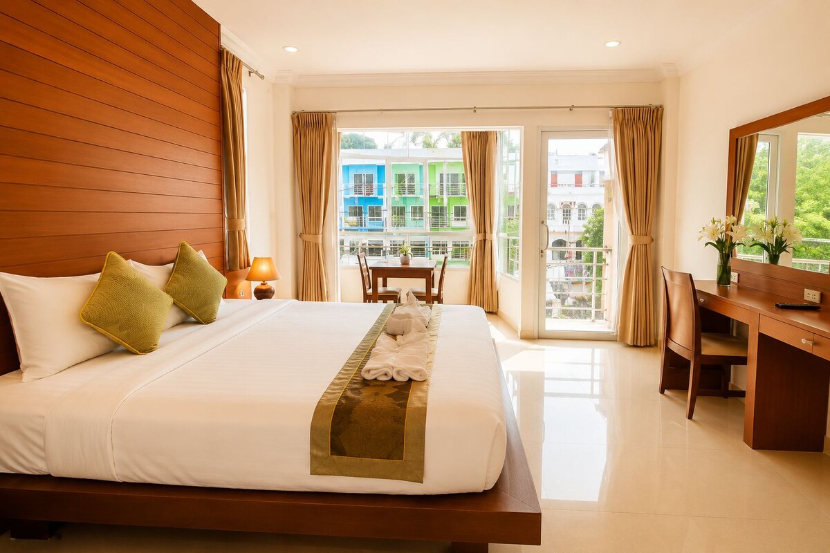 A hotel room with a large bed, a desk, and a view of buildings through the window.