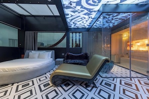 Habitación de hotel moderna con cama, sillón, ventana grande y diseño de techo original.