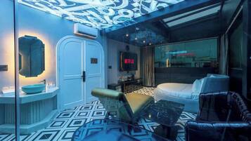 Una habitación de hotel moderna con piso de diseño geométrico, un sofá, una mesa de centro, un televisor y un techo con iluminación decorativa.