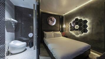A modern hotel room with a large bed, a round wall mirror, and a unique hexagonal light fixture.
