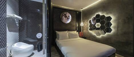 Une chambre d’hôtel moderne dotée d’un grand lit, d’un miroir rond fixé au mur et d’un luminaire hexagonal original.