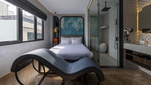 A modern bedroom with a curved bench, a bed, a glass shower, and a view of the city. - PYNT Hotel (Ho Chi Minh City)