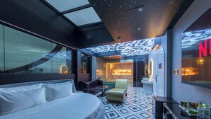 A modern hotel room with a large bed, a seating area, and a view of the cityscape through large windows. - PYNT Hotel (Ho Chi Minh City)