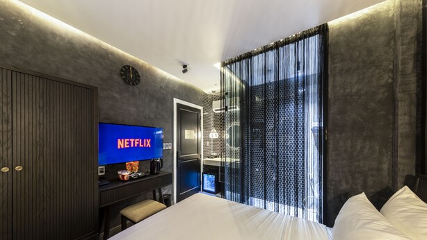 A modern hotel room with a large bed, a flat-screen TV displaying Netflix, a desk with a coffee machine, and a wardrobe. - PYNT Hotel (Ho Chi Minh City)