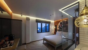 A modern hotel room with a bed, a desk with a coffee maker, a window, and a glass partition. - PYNT Hotel (Ho Chi Minh City)