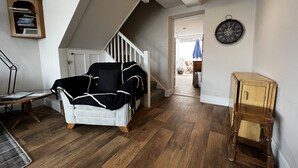 A room with a white sofa, wooden flooring, a staircase, and a clock on the wall. - Bell Cottage (Cowes)