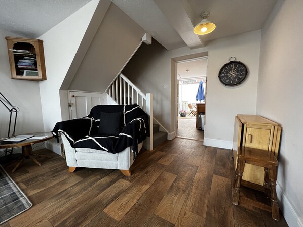 A room with a white sofa, wooden flooring, a staircase, and a clock on the wall. - Bell Cottage (Cowes)