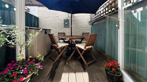 A wooden deck with a table and chairs, a blue umbrella, and potted plants. - Bell Cottage (Cowes)