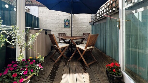 A wooden deck with a table and chairs, a blue umbrella, and potted plants. - Bell Cottage (Cowes)