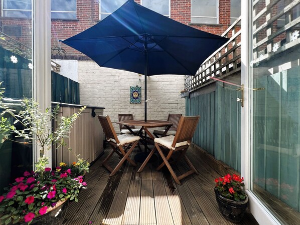 A wooden deck with a table and chairs, a blue umbrella, and potted plants. - Bell Cottage (Cowes)