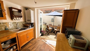A kitchen with wooden cabinets, a sink, a stove, and a dining area with a table and chairs. - Bell Cottage (Cowes)