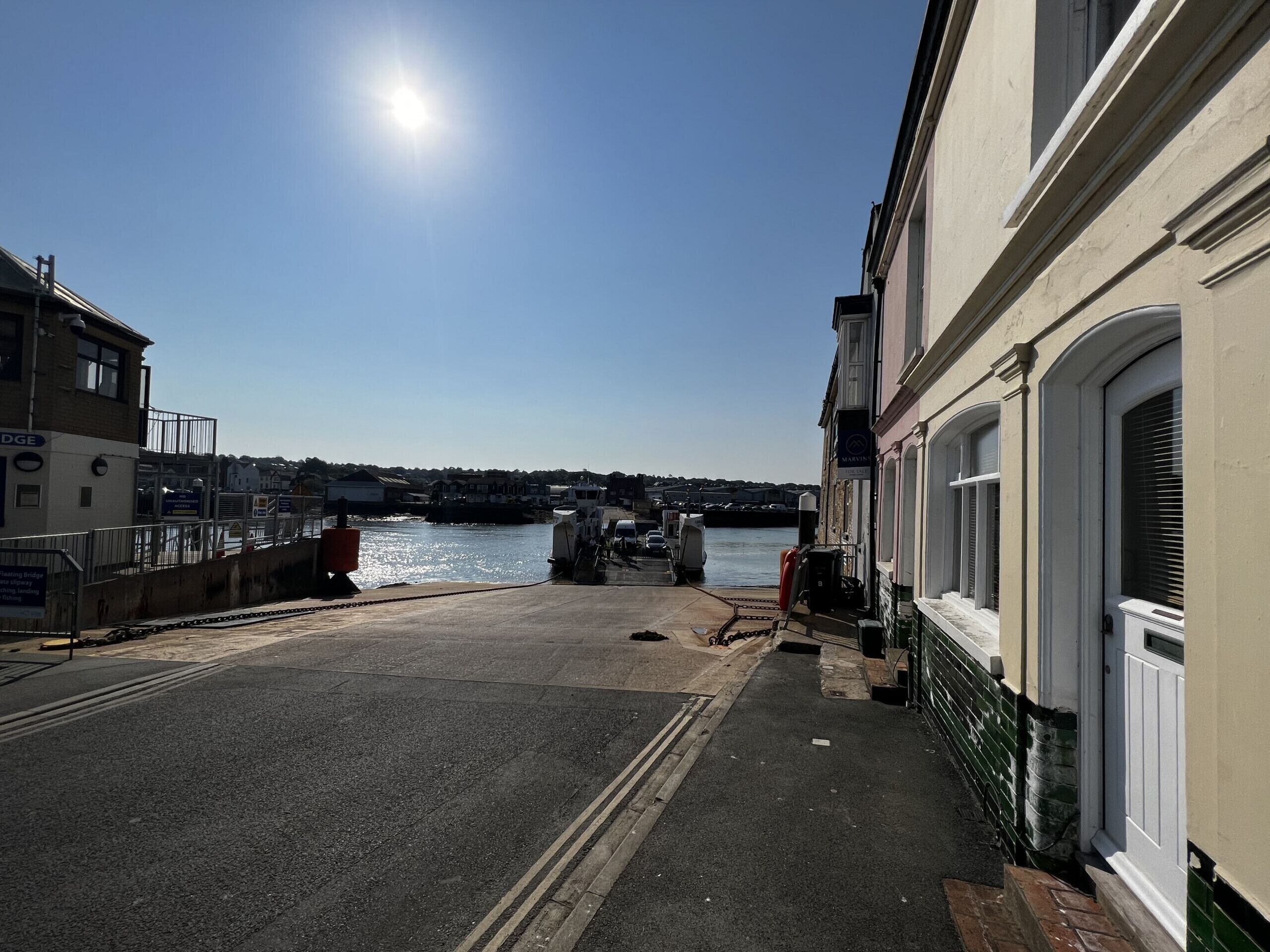 A waterfront street with buildings on either side, a clear sky, and a calm water body in the background.