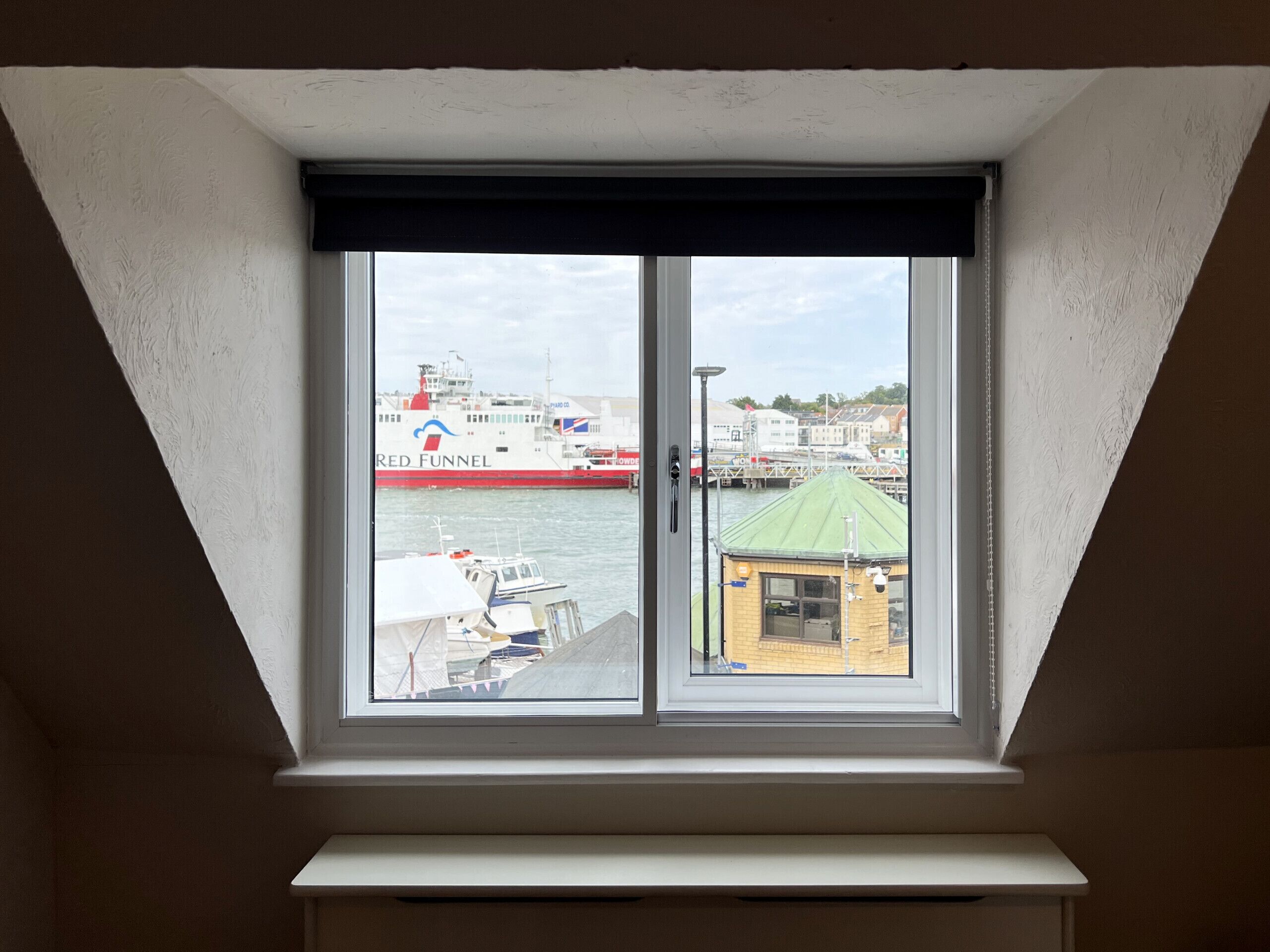 A window with a view of a harbor, including a large ship and a small building.