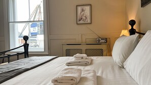 A neatly made bed with folded towels, a radio on a bedside table, and a framed artwork on the wall. - Bell Cottage (Cowes)