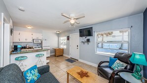 A compact living space with a kitchenette, a dining area, a seating area with a coffee table, and a TV mounted on the wall. - Come and enjoy Beachside villa suite #2   Steps from BEACH (Indian Rocks Beach)
