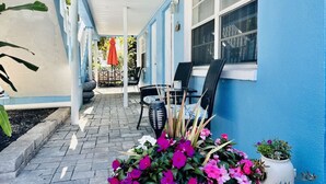 A covered patio area with a blue exterior wall, a brick floor, and outdoor furniture including two chairs and a table. - Come and enjoy Beachside villa suite #2   Steps from BEACH (Indian Rocks Beach)