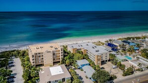 A coastal hotel with multiple buildings, a parking area, and a beach in the background. - Come and enjoy Beachside villa suite #2   Steps from BEACH (Indian Rocks Beach)