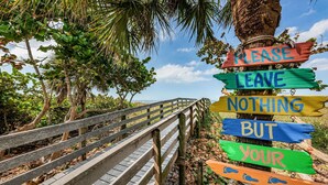 A wooden boardwalk with a signpost featuring colorful signs that read "PLEASE LEAVE NOTHING BUT YOUR FOOTPRINTS." - Come and enjoy Beachside villa suite #2   Steps from BEACH (Indian Rocks Beach)
