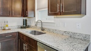 A kitchen with dark wooden cabinets, a granite countertop, a stainless steel sink, and a built-in dishwasher. - Downtown - Coastal Cozy 3B Home! (Pensacola)