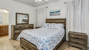 A bedroom with a wooden bed, a nightstand, a dresser, a ceiling fan, and a painting on the wall. - Downtown - Coastal Cozy 3B Home! (Pensacola)
