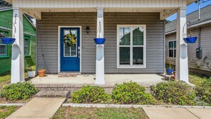A residential house with a blue front door, a porch with a white railing, and a small garden area. - Downtown - Coastal Cozy 3B Home! (Pensacola)