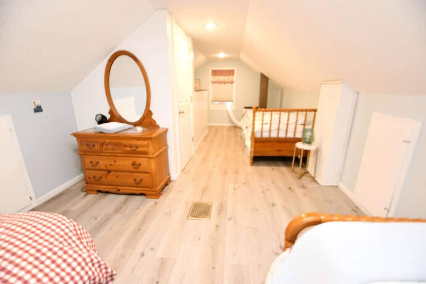 A bedroom with a wooden dresser, a mirror, a crib, and a checkered bedspread.