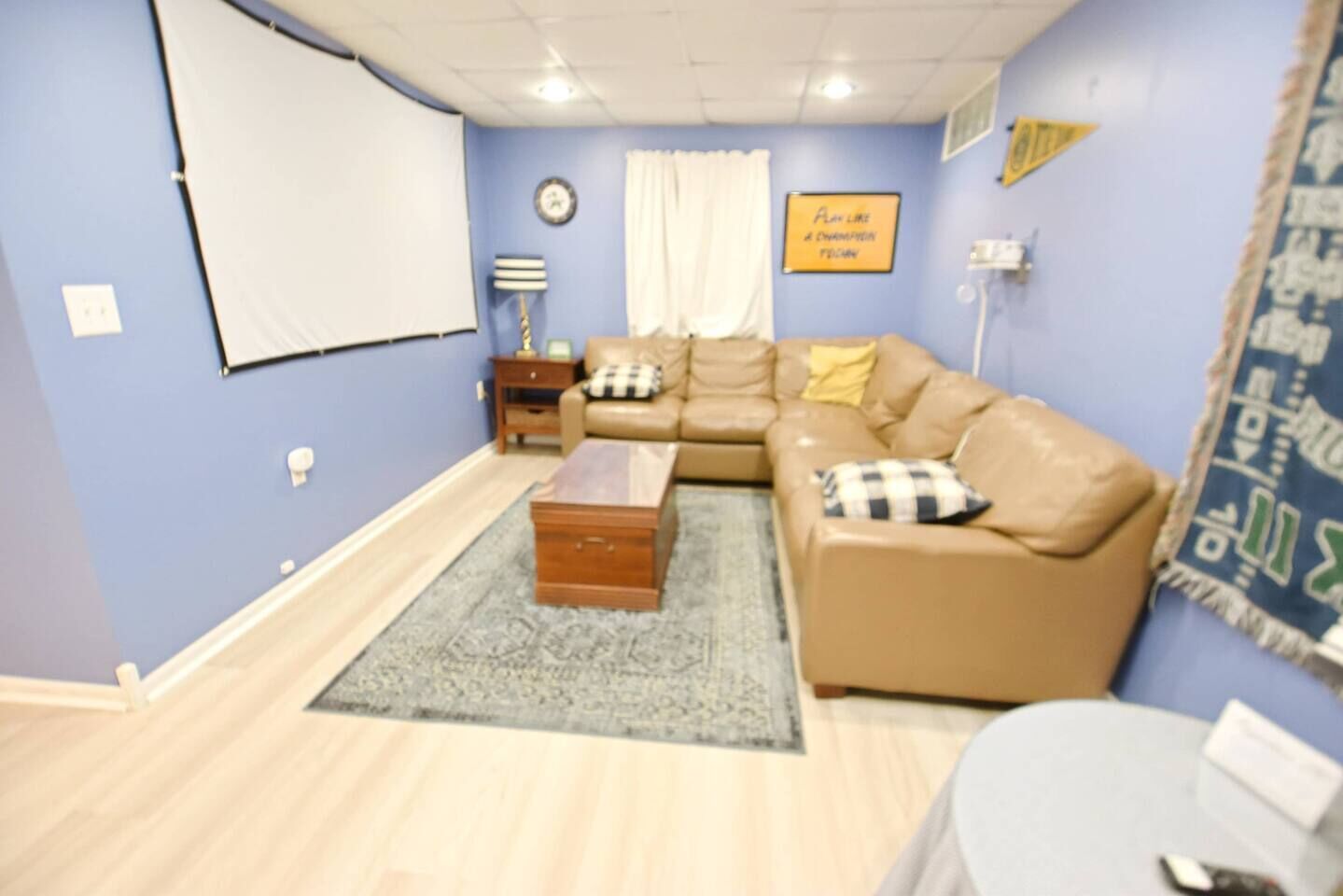 Una sala de estar con un sofá modular, una mesa de centro, una alfombra, un reloj y una pantalla de proyector instalada en la pared.