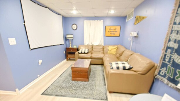 Una sala de estar con un sofá modular, una mesa de centro, una alfombra, un reloj y una pantalla de proyector instalada en la pared.