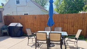 Un patio al aire libre con mesa y sillas, una parrilla cubierta y un cerco de madera.