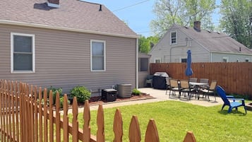 A residential backyard with a wooden fence, a patio with outdoor furniture, and a covered grill area.