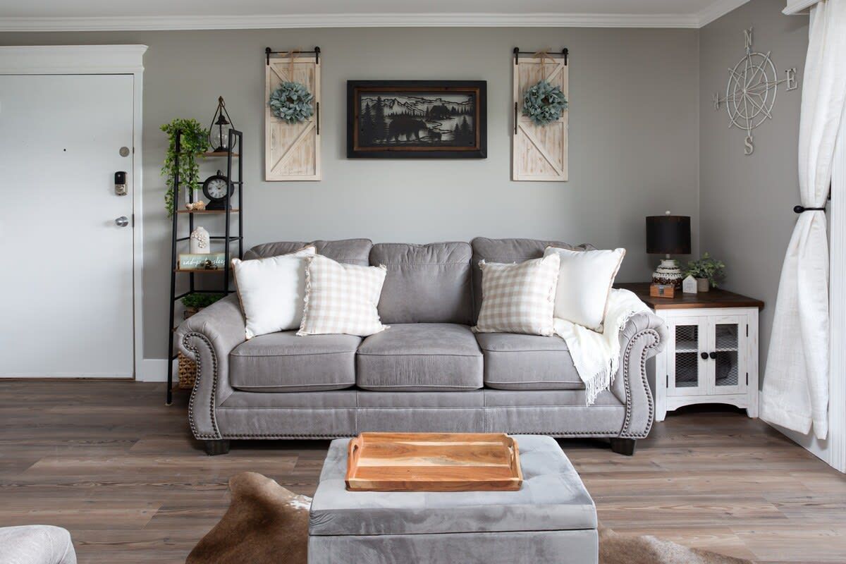 A living room with a grey sofa, a wooden side table, and a decorative wall piece.
