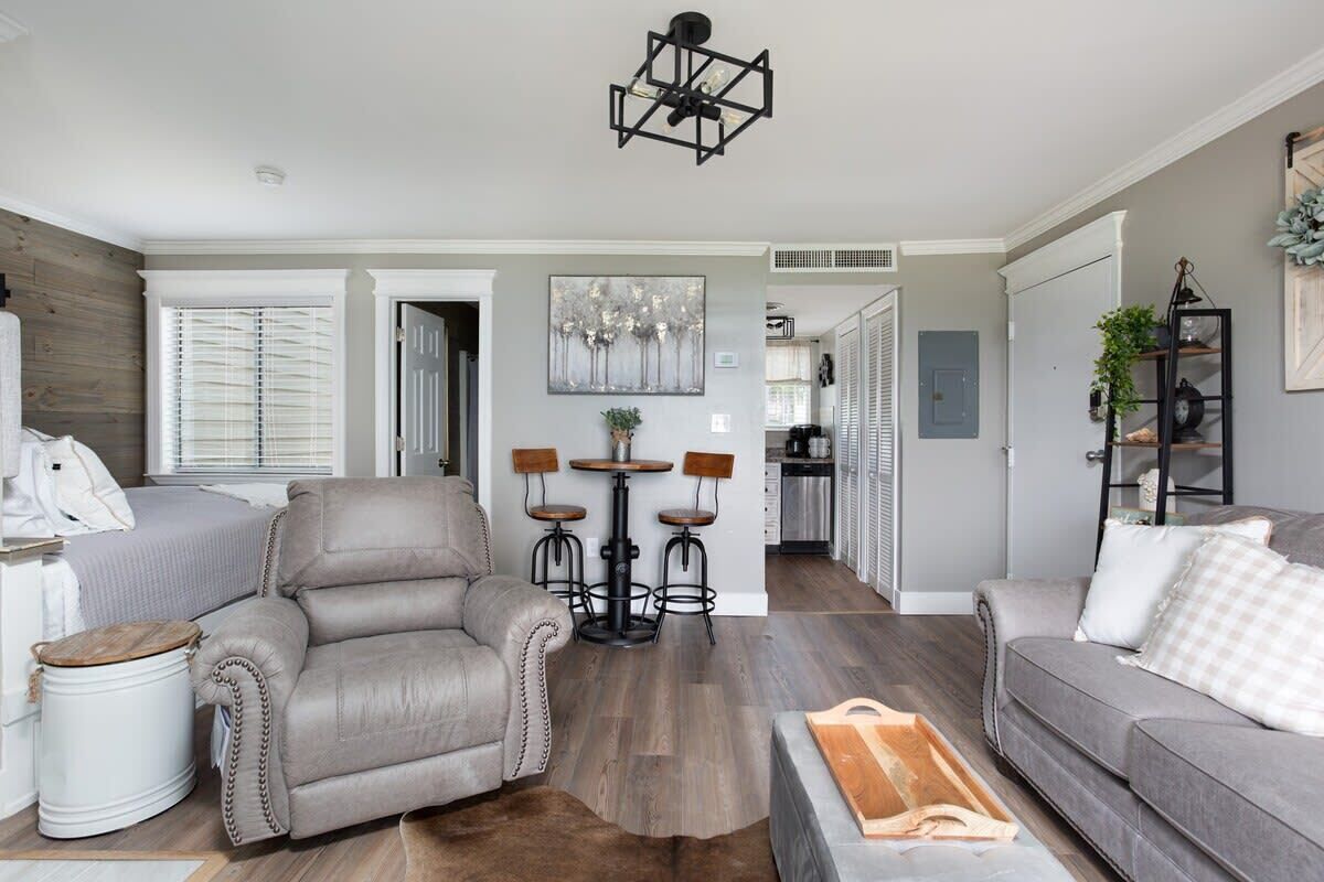 A modern living room with a leather armchair, a grey sofa, and a dining area with stools.