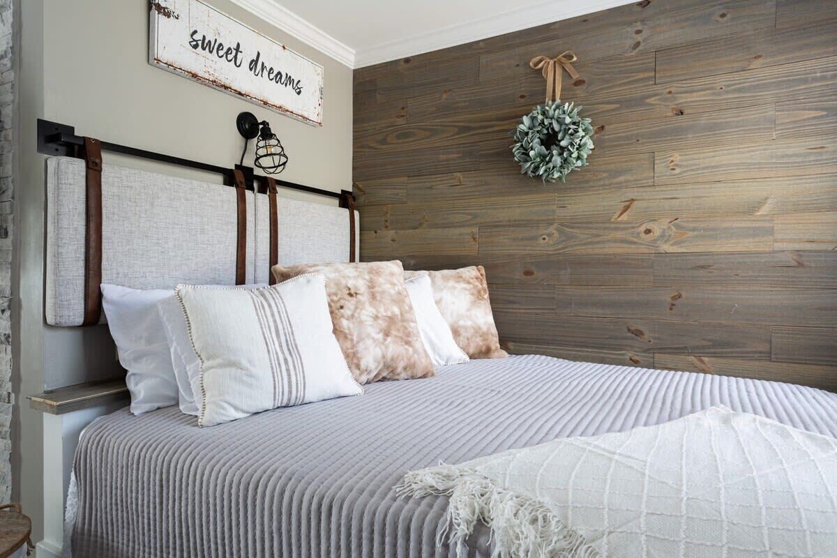 A bedroom with a bed, pillows, a headboard, a wall-mounted sign, and a wreath.