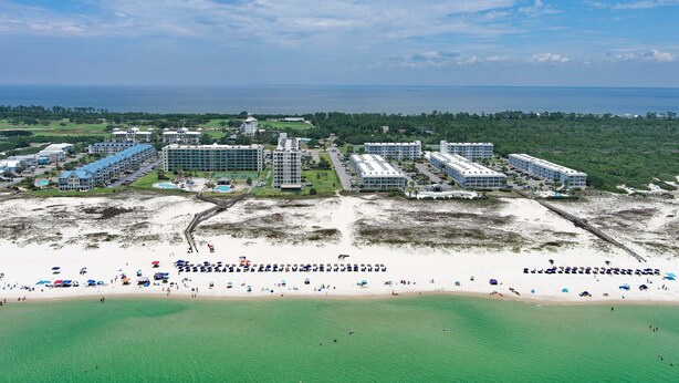 A coastal hotel with multiple buildings, a beach with umbrellas, and a view of the sea. - Beach Please 2BR Gulf Shores Oceanfront/Pool, Beach Please Beachfront condo sleeps 6 (Baldwin County)