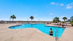A swimming pool with a curved edge, surrounded by lounge chairs and palm trees. - Beach Please 2BR Gulf Shores Oceanfront/Pool, Beach Please Beachfront condo sleeps 6 (Baldwin County)