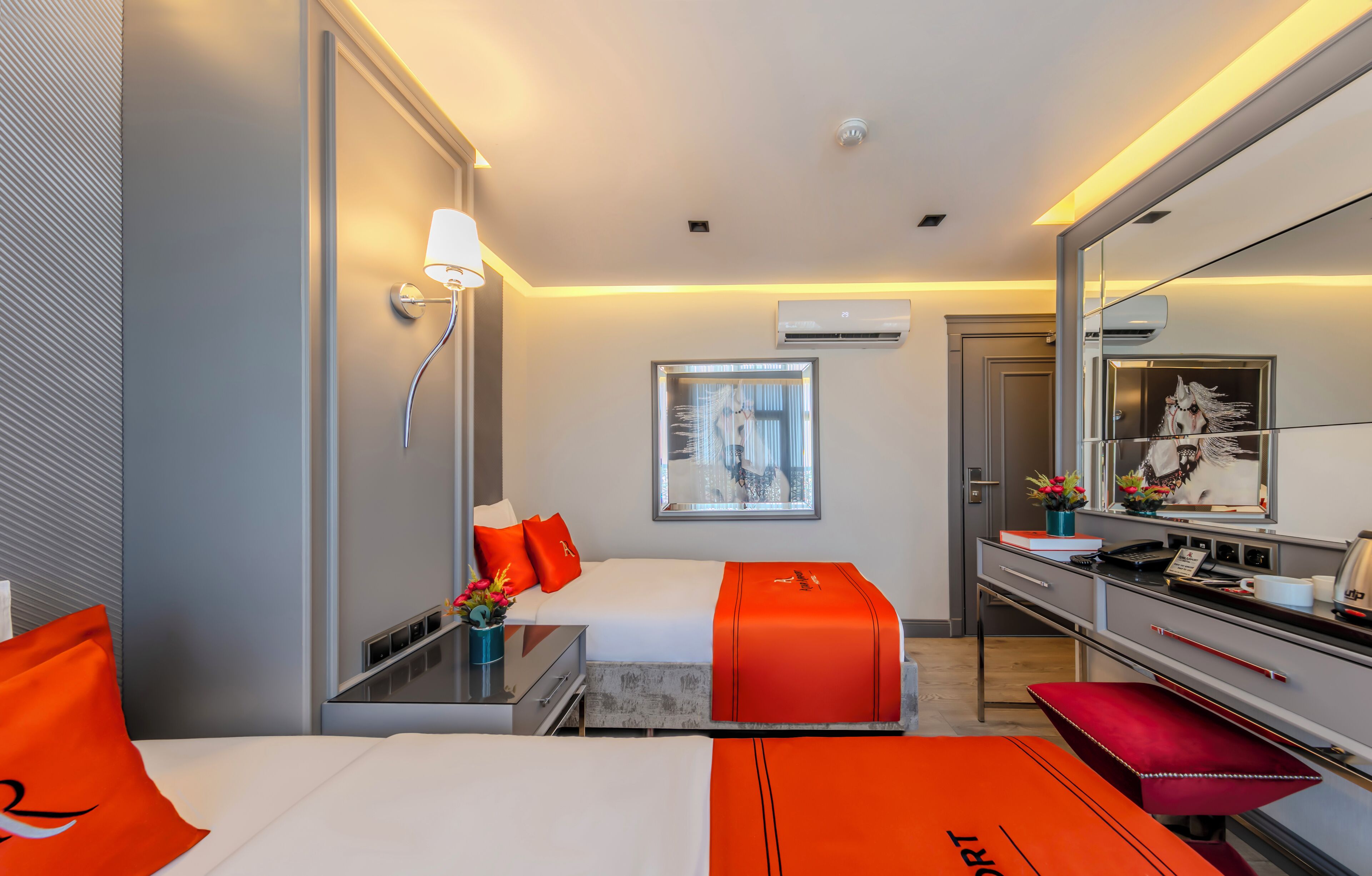 A modern hotel room with a bed, a desk, a chair, a mirror, and a window with curtains.
