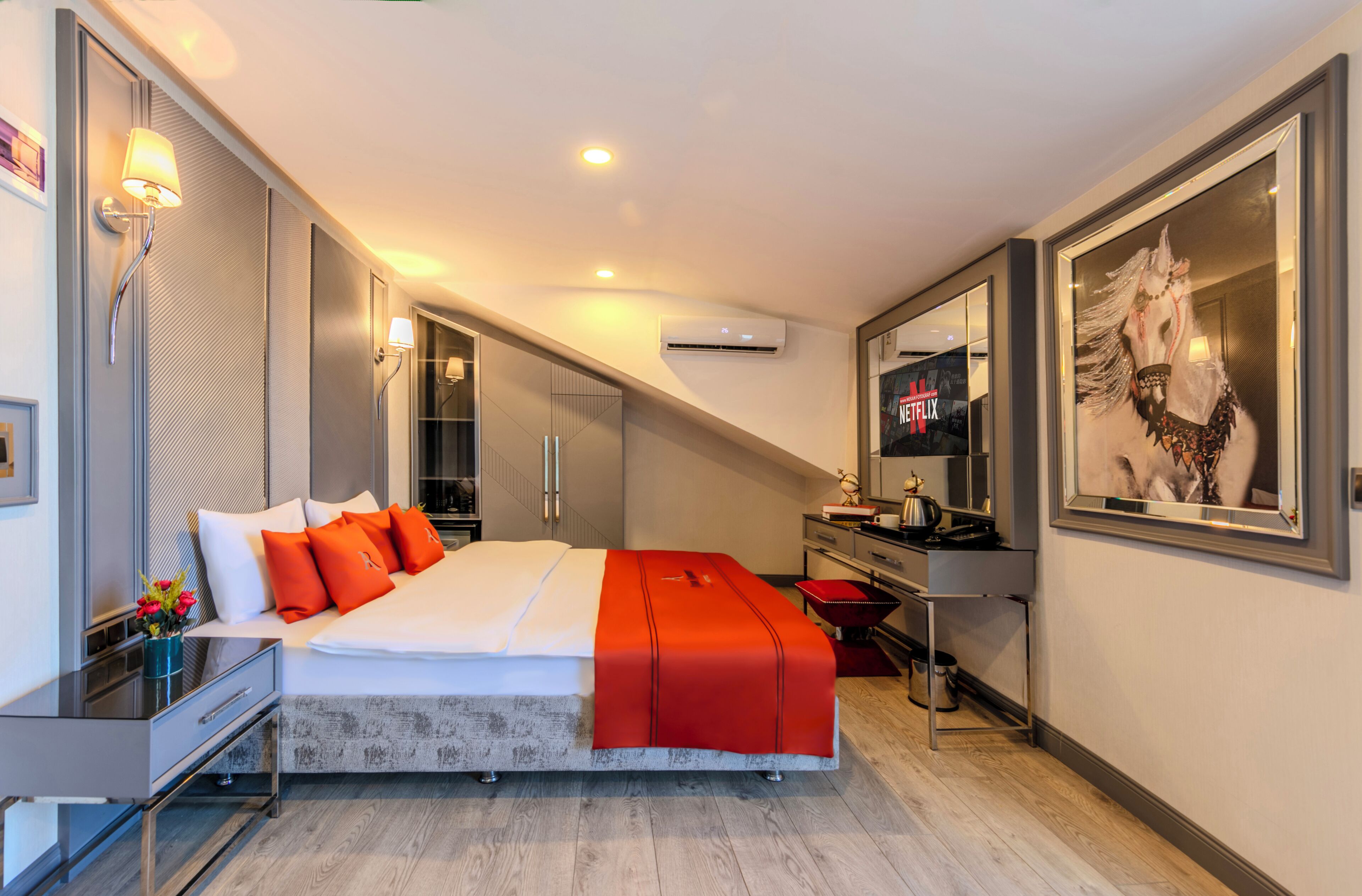 A modern hotel room with a large bed, a desk, a mirror, and a TV.