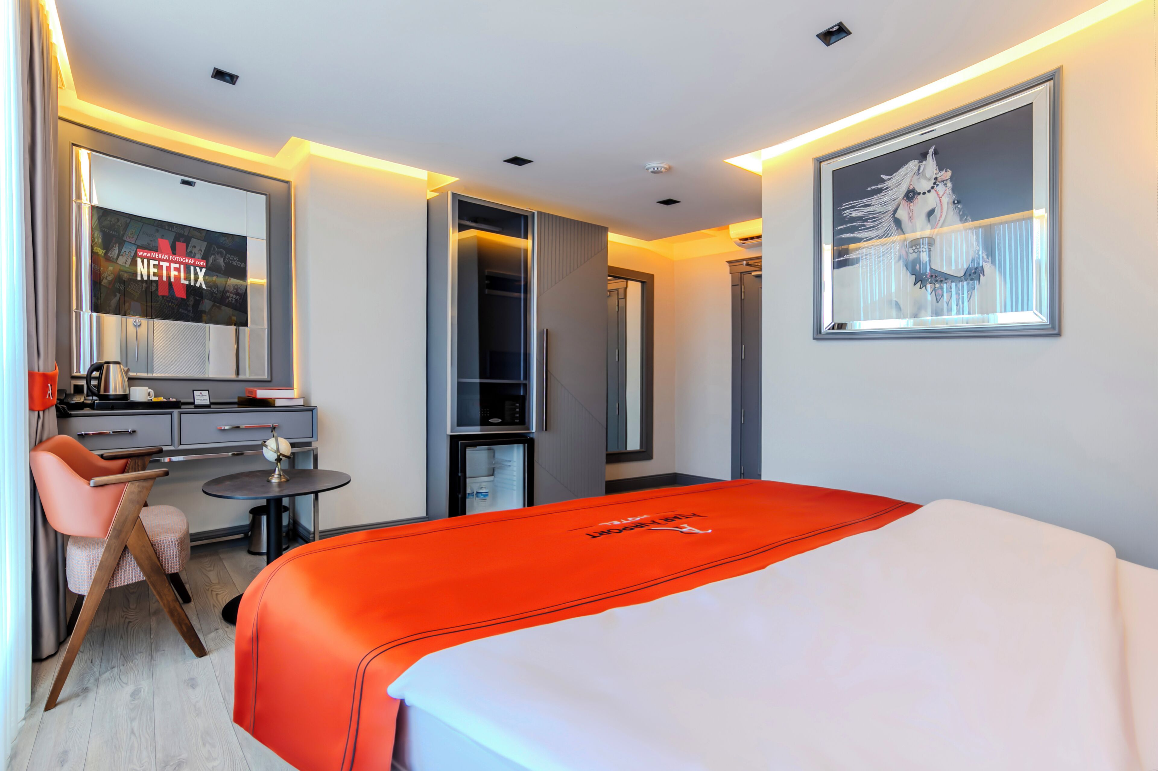 A hotel room with a bed, a desk, a chair, a small table, a TV, and a framed picture on the wall.