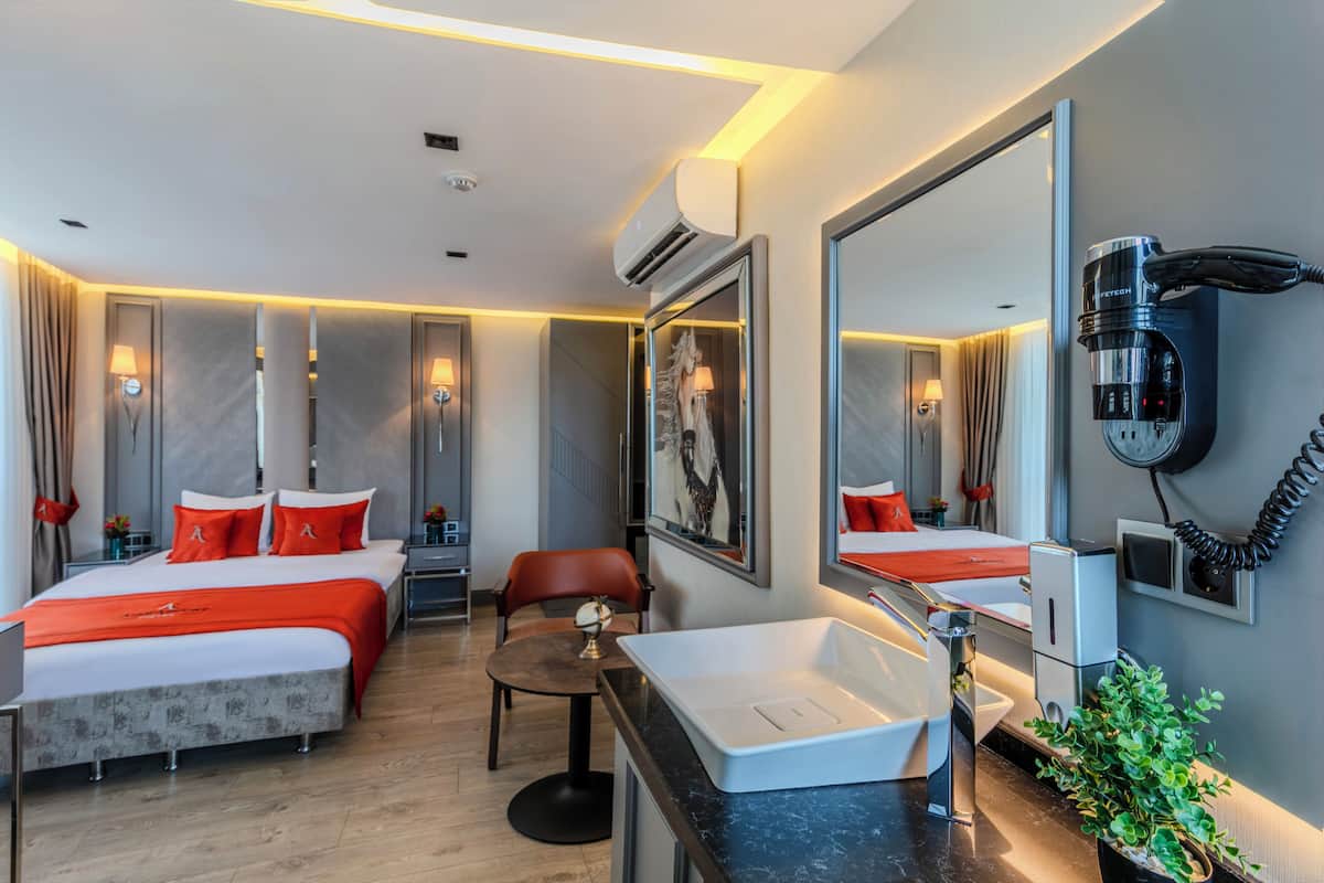 Una habitación de hotel moderna con dos camas, una zona de estar, un espejo grande, un secador de pelo y un lavamanos.