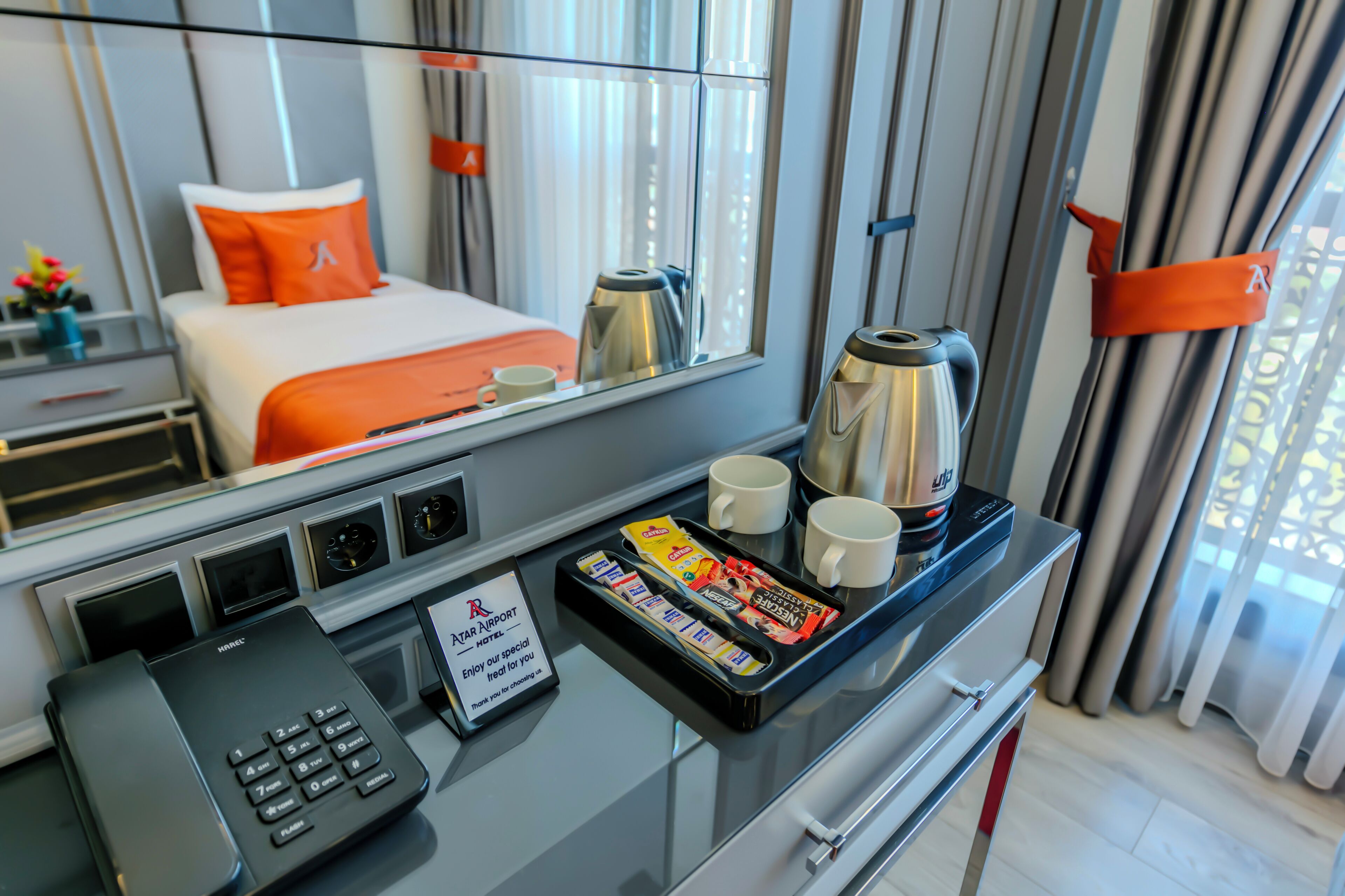 A hotel room with a bed, a coffee maker, a tray with snacks, a phone, and a sign.