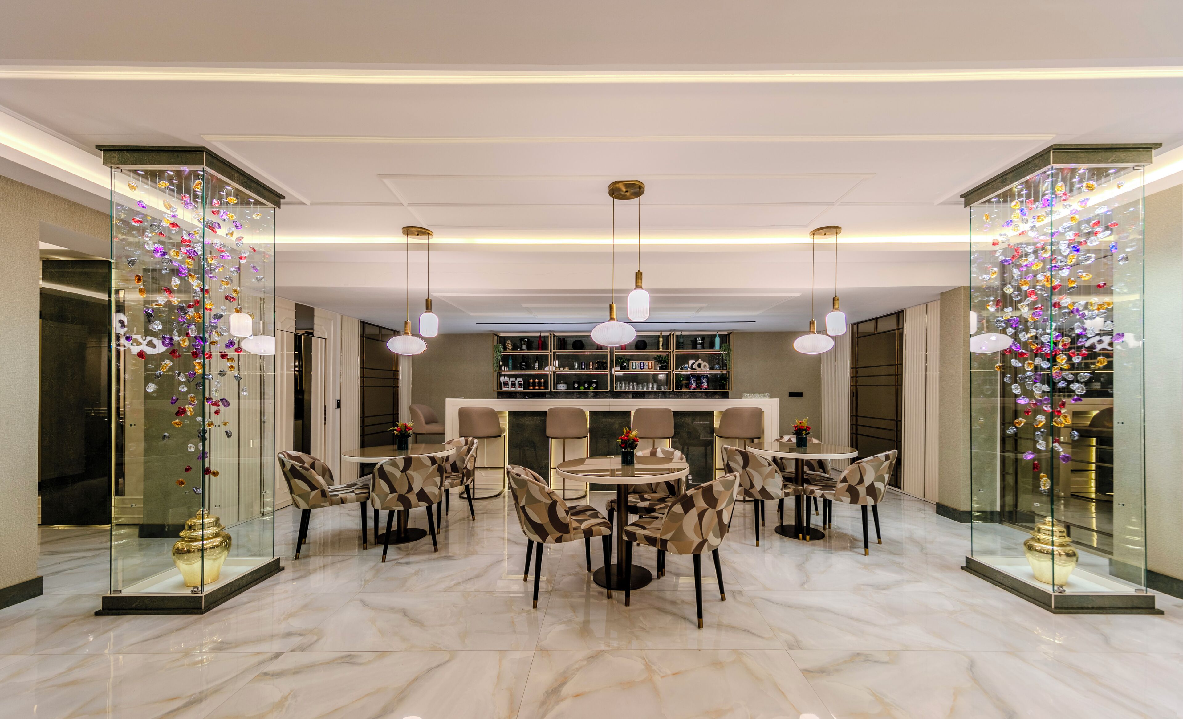 A modern dining area with a central round table, surrounded by patterned chairs, and glass display cases with decorative items on either side.