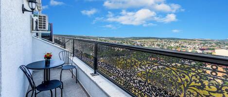 A balcony with a table and chairs, a decorative railing, and a view of a town.