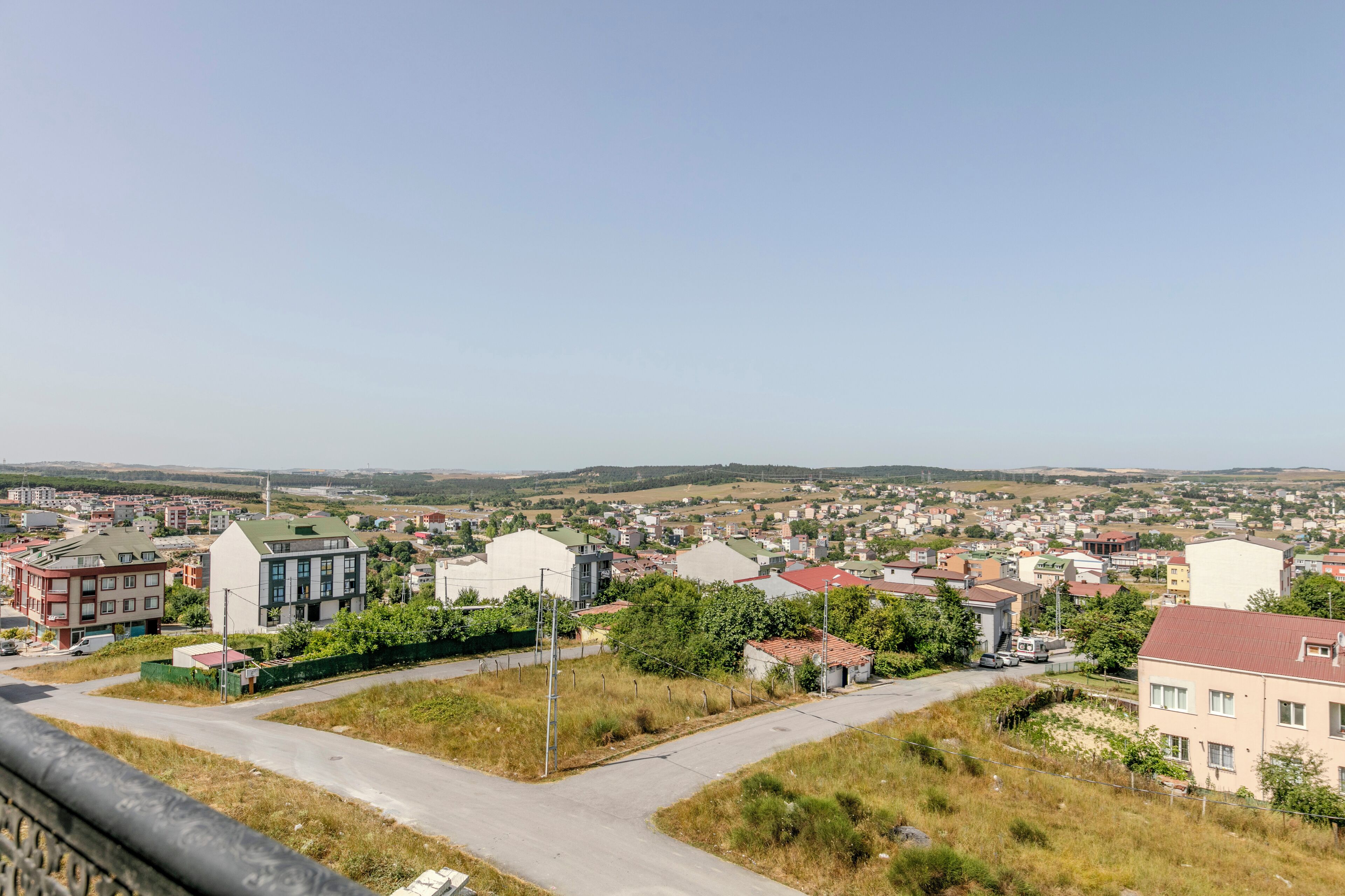 A residential area with a mix of modern and traditional buildings, a clear sky, and a distant view of hills.