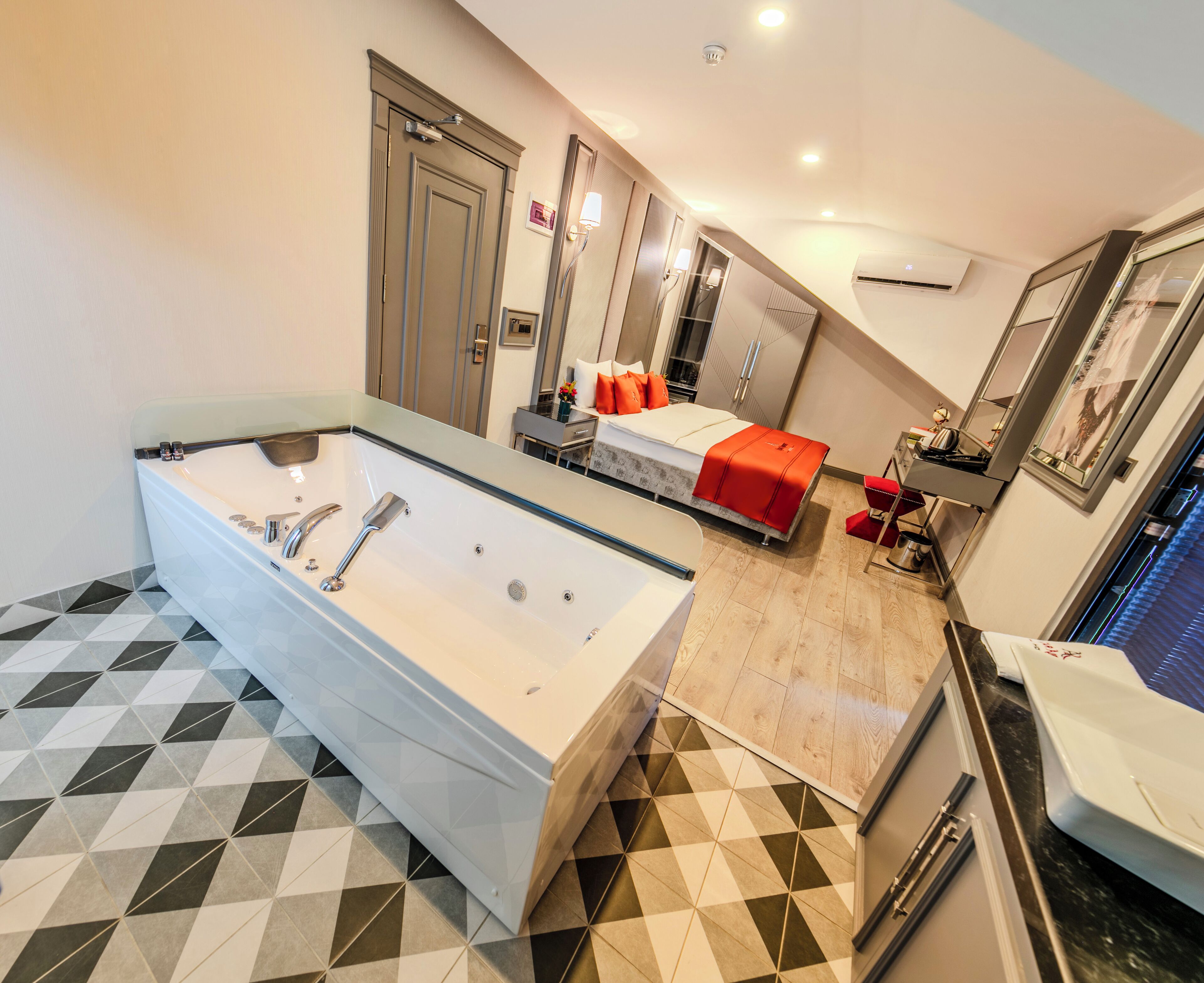 A modern bathroom with a large bathtub, a separate shower area, and a bed with red bedding.