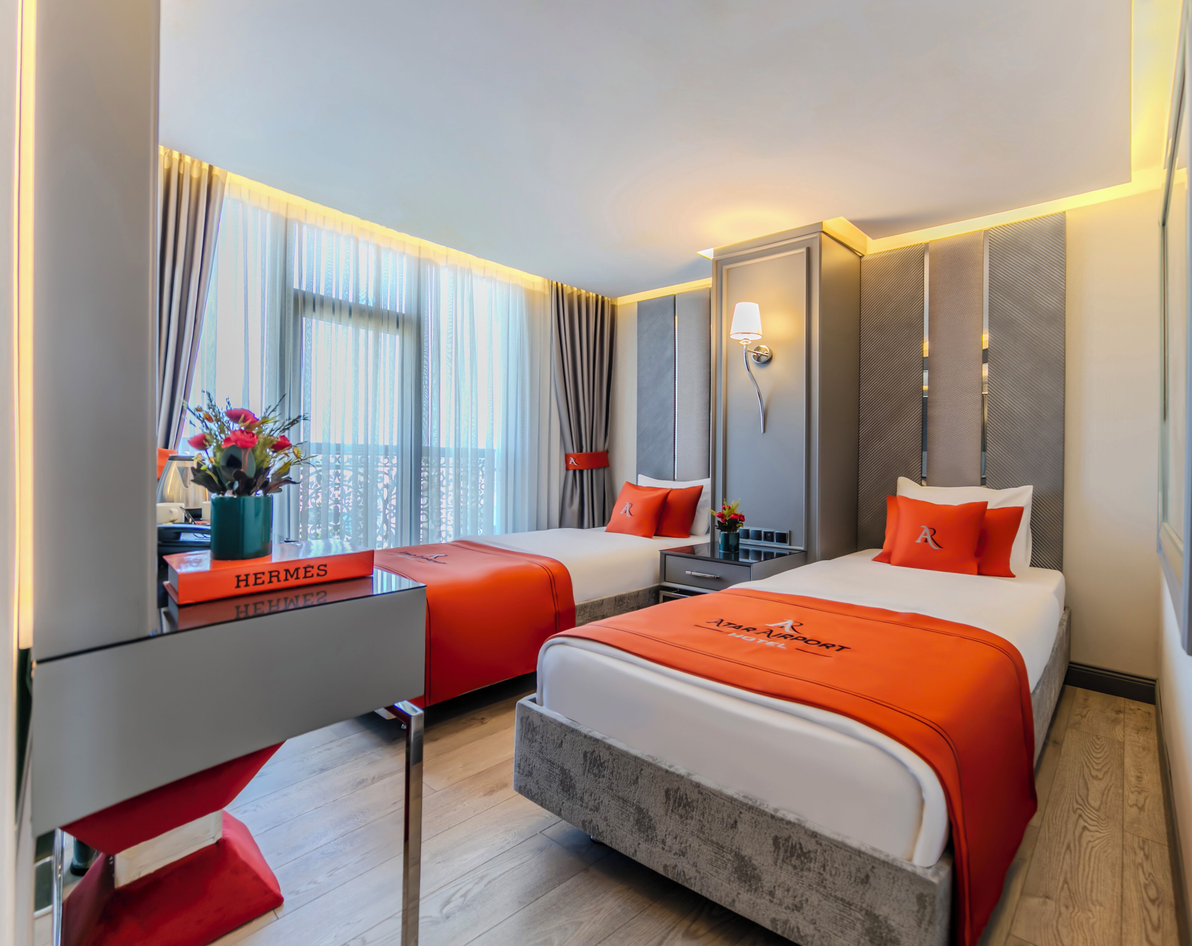 A hotel room with two beds, a desk, and a window with curtains.