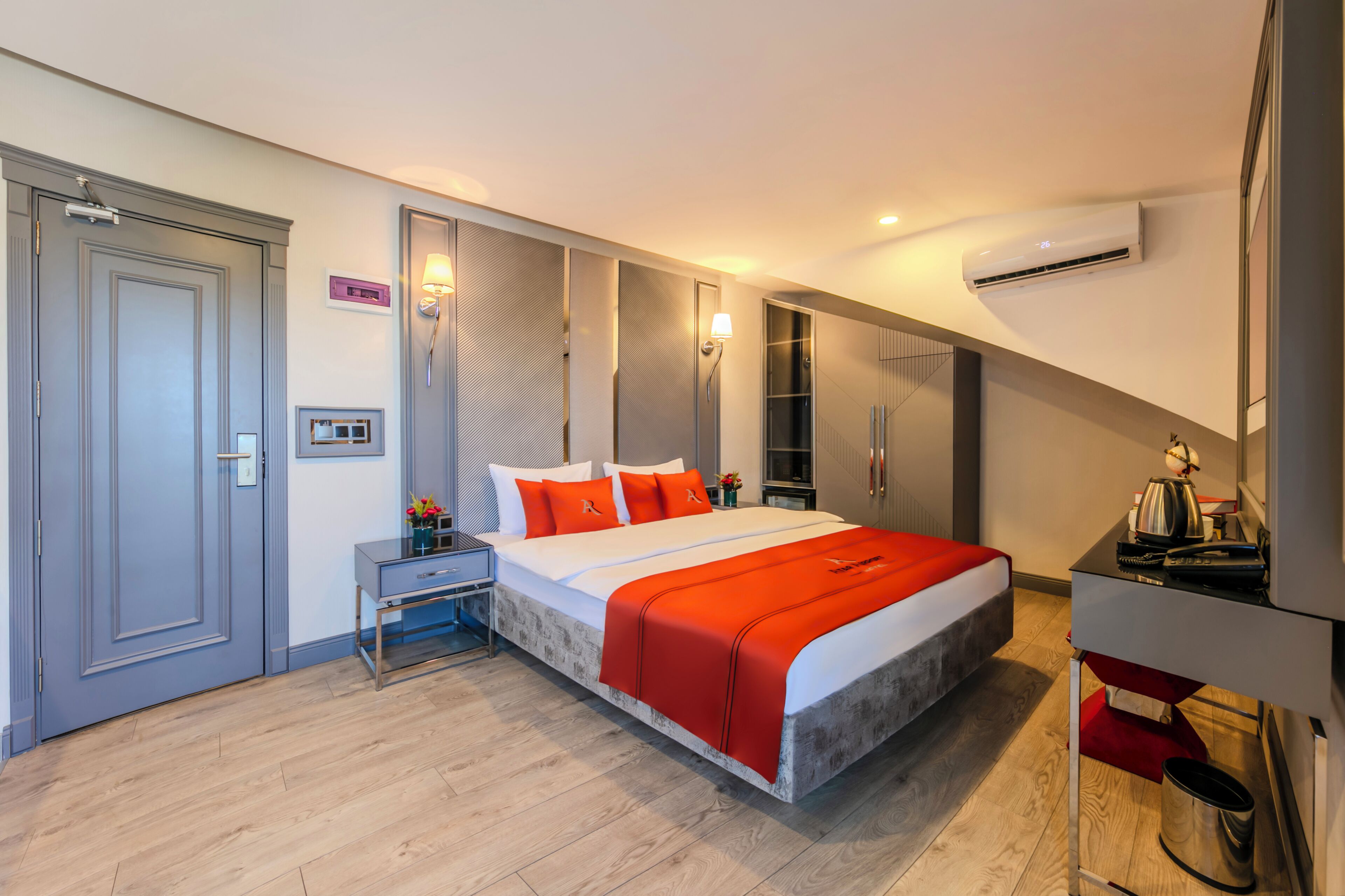 A modern hotel room with a large bed, a desk, a wardrobe, and an air conditioning unit.