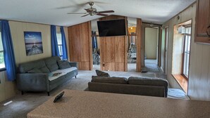 A living room with a grey sofa, a brown couch, a TV mounted on a wooden wall, and a ceiling fan. - Gateway to keystone lake, Jellystone park , new mannford ramp& the harbor . (Mannford)